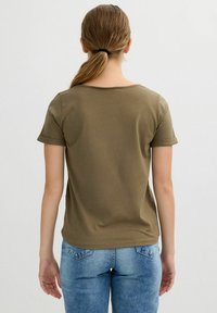 Camiseta de color verde oliva, de manga corta, con un cuello redondeado y los puños enrollados, combinada con unos vaqueros de mezclilla azul claro. Material de algodón suave.