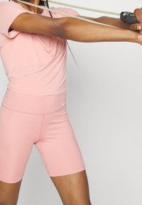 Top deportivo rosa y pantalones cortos ajustados a juego, hechos de tela elástica, con una textura sutil y el logo de Nike en la cintura.