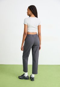 Grijze crop top, rechte donkergrijze broek met achterzakken, en zwarte sneakers met witte sokken, gezien vanaf de achterkant op groene vloer.