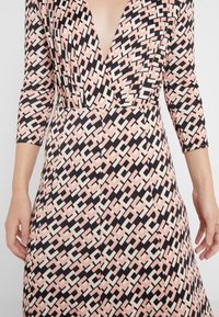 Šaty s dlouhým rukávem z měkké látky s hlubokým výstřihem do V. Černé pozadí s geometrickými vzory v růžových a krémových odstínech, přiléhavý střih.