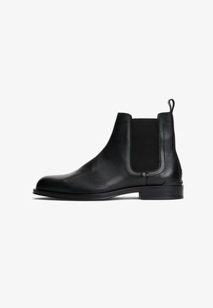 Black leather Chelsea boots with elastic side panels, rounded toe, flat sole, and pull tab at the back for easy wear. Smooth texture.