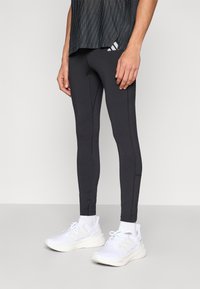 Leggings deportivos negros con una textura suave y detalles de costuras, combinados con zapatillas blancas que presentan paneles de malla y sólidos.