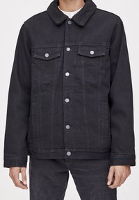 Veste en denim noire avec un col duveteux, deux poches poitrine et une fermeture à boutons sur le devant. Caractérisée par une coupe décontractée et des détails de couture subtils.