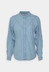 Ljusblå denimblus med långa puffärmar, knapfront, rund krage och diagonala sömdetaljer över bröstet.