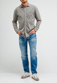 Grijze lange mouwen button-up shirt met een borstzak, gecombineerd met blauwe spijkerbroek en grijze sneakers. Eenvoudig ontwerp met een relaxte pasvorm.