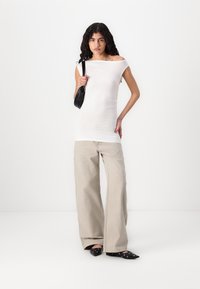 Haut blanc à épaules dénudées ajusté, pantalon beige àjambe large, sac à main noir et chaussures noires à bouts pointus avec des accents circulaires. Tissu lisse et léger.