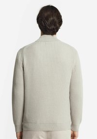 Ljust grå ribbad stickad tröja med en åtsittande krage och långa ärmar, med ett strukturerat mönster över hela.