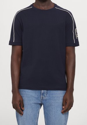 Granatowy bawełniany t-shirt z białym przeszyciem przy ramionach. Posiada krótkie rękawy i okrągły dekolt. Logo marki na rękawie.