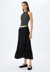 Mustapohjainen crop-top, jossa on valkoiset raidat, yhdistettynä mustaan, liehuvaan nilkkapituiseen kietaisuhameeseen, jossa on röyhelöhelma. Yhdistetty mustiin ballerinoihin.