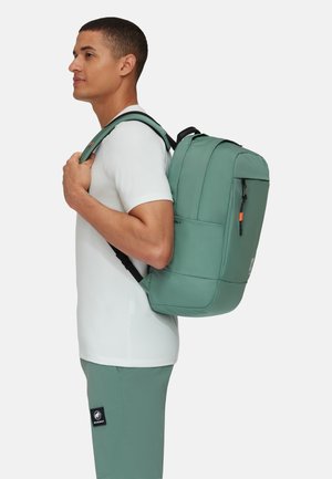 Mochila verde hecha de material duradero, con correas acolchadas, un bolsillo frontal y un compartimento principal espacioso. Textura suave, diseño minimalista.