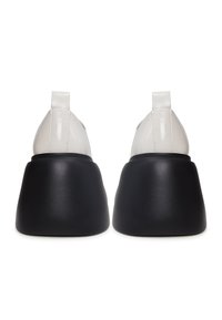 Adidași din piele albă cu tălpi din cauciuc negru, având texturi fine și un design elegant, dotati cu mici bucle pe călcâie pentru o îmbrăcare ușoară.