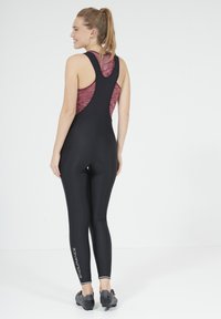 Zwarte fiets-broek met bretels en een mouwloos bordeauxrood top, met een racerback ontwerp en reflecterende accenten. Tekst "ENDURANCE" langs het been.