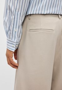 Beezhised püksid tagataskuga, kombineeritud helesinise ja valge triibulise särgi, millel on nööpidega mansetid. Sile kangas on nähtav.