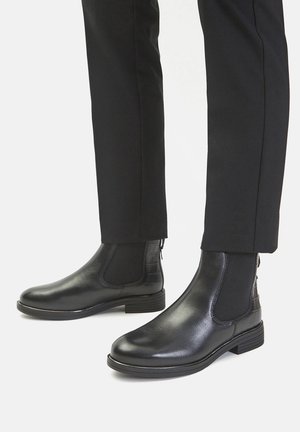 Czarne skórzane buty Chelsea z elastycznymi panelami po bokach, gładką fakturą i niskim, masywnym obcasem, z delikatnymi bocznymi akcentami.