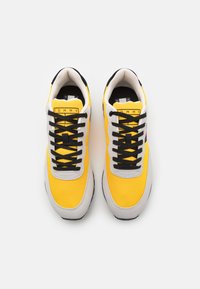 Sneaker gialle e grigie con lacci neri. Presentano un upper testurizzato, un colletto imbottito e l'etichetta del marchio sulla linguetta. Suola in gomma.