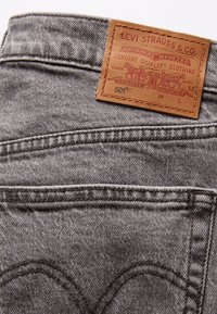 Jeans de mezclilla grises con un parche de cuero marrón etiquetado "Levi Strauss & Co." Presenta bolsillos traseros distintivos y detalles de costura sutiles.