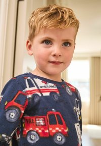 Niebieska bluzka piżamowa z polaru z kolorowymi wzorami wozów strażackich i ambulansów. Model z okrągłym dekoltem, krótkimi rękawami i miękką teksturą.