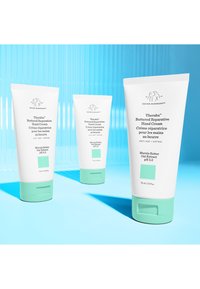 Three white tubes of Drunk Elephant Therabru™ Buttered Reparative Hand Cream, featuring mint green accents and a minimalist design.