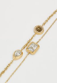Bracciale color oro con tre pezzi decorativi: un ciondolo circolare con pietre trasparenti, una pietra a forma di pera simile a un diamante e una gemma rettangolare.