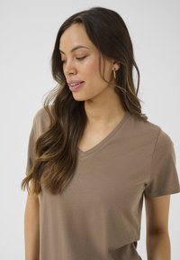 T-shirt marron à manches courtes et décolleté en V, fabriqué en tissu doux, avec une coupe décontractée et une texture sans couture, ornée d'un ourlet légèrement arrondi.
