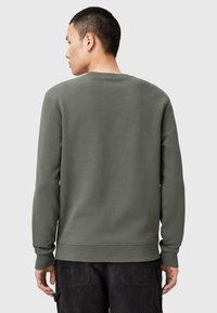 Sudadera gris de manga larga, cuello redondo y puños acanalados. Textura suave, corte relax, diseño sencillo sin patrones visibles.