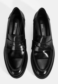 Schwarze Lederloafers mit glänzender Oberfläche, einem breiten Riemen mit einem dezenten V-Ausschnitt und einer stabilen Gummisohle, die ein elegantes, minimalistisches Design präsentieren.