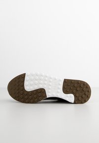 Schwarze Schuhsohle mit einem weißen und braunen strukturierten Design, das erhöhte runde Griffe für Traktion aufweist und den Markennamen auf der Oberfläche eingeprägt hat.