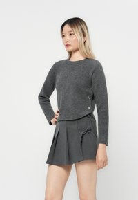 Grå strikkegenser med rund hals, lange ermer og dekorative knapper på siden, sammen med et grått plissert skjørt med knyting.