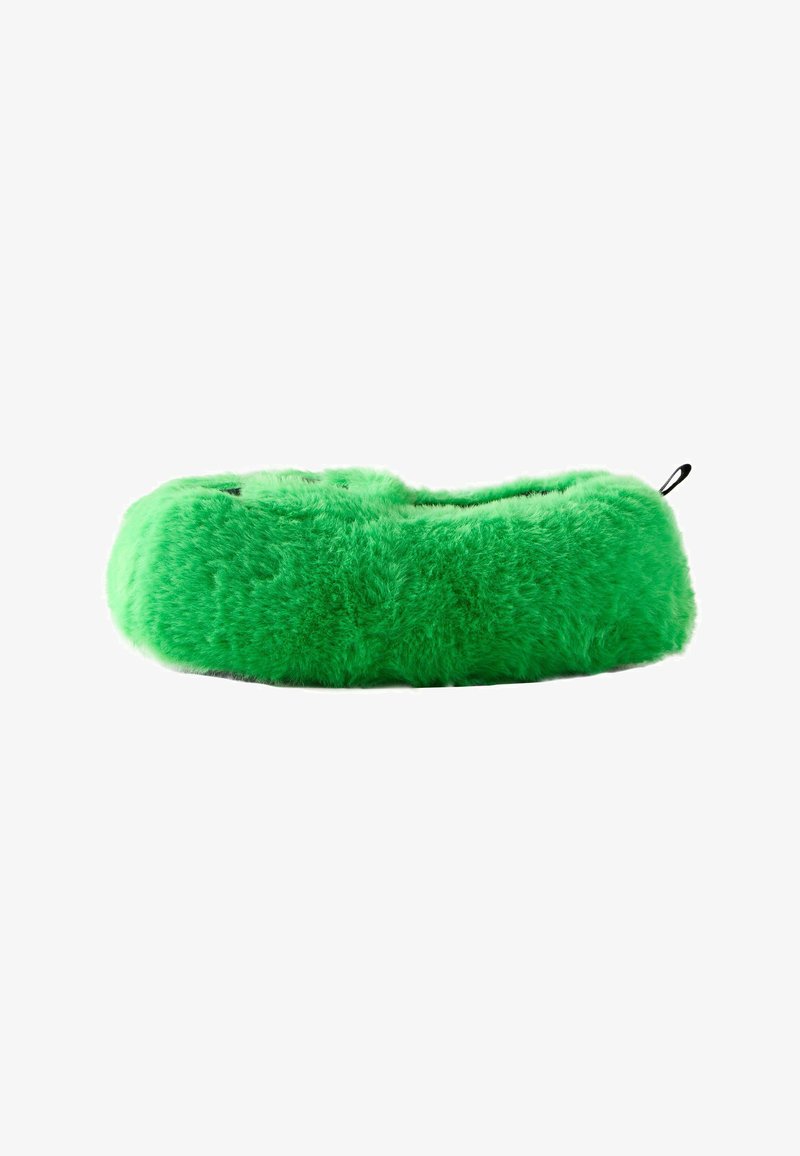Chausson pelucheux vert vif avec un bout arrondi et une petite languette noire au talon sur fond blanc.
