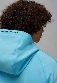 Felpa con cappuccio azzurro chiaro con cordoncino, presenta un logo distintivo "Jordan Sport" in nero vicino al collo. Tessuto liscio con cuciture visibili.