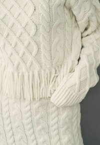 Off-white stickad tröja med flätmönster, ribbade ärmar och en fransad nederkant. Mjuk textur med en lös och avslappnad passform.