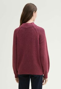 Rippstrickpullover in dunkelrosa mit langen Ärmeln, hohem Kragen und lockerer Passform, mit kontrastierenden vertikalen Streifen.