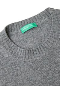 Pull en tricot gris avec un col rond côtelé ; présente une étiquette verte portant la mention "UNITED COLORS OF BENETTON". Texture lisse, design décontracté.