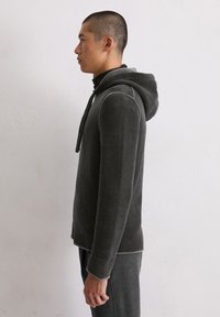 Grijze hoodie gemaakt van gestructureerde stof, met een kangoeroezak en contrasterende stiksels langs de naden.