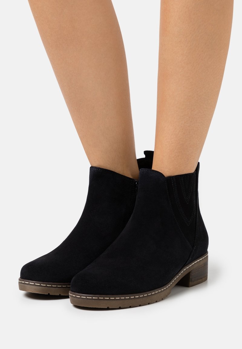 Bottines en daim noir avec un bout rond, des panneaux latéraux élastiques texturés et un petit talon en bois. Présentent des coutures décoratives sur les côtés.