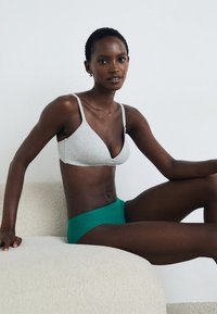 Braletă wireless gri cu un design triangular și bretele ajustabile, asortată cu chiloți verzi cu talie înaltă. Textură netedă, stil minimalist.