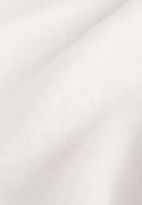 Weißer Leinenstoff mit einer weichen, strukturierten Oberfläche, leichtem Glanz und dezentem Webmuster, der in sanften Falten drapiert ist.