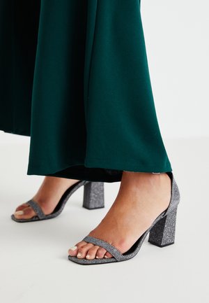 Hõbedased sädeleva bloki-kontsa sandaalid, millel on kaks õhukest rihma ja ruudukujuline varvas. Kaasas tumeroheline põrandale ulatuv rõivas.