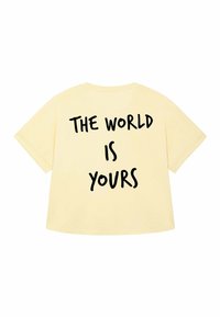 T-shirt giallo chiaro con vestibilità comoda, caratterizzato da un grande testo nero sulla schiena che recita "IL MONDO È TUO." Materiale in cotone, maniche corte.