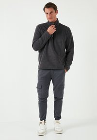 Grauer Fleece-Halfzip-Pullover mit einem strukturierten Oberflächen, kombiniert mit schmal zulaufenden Cargo-Hosen in Dunkelgrau mit seitlichen Taschen, getragen mit weißen Sneakers.