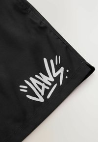 Sorte badebukser med et hvidt grafisk print af ordet "JAWS" med dynamiske accenter, lavet af letvægts, hurtigtørrende stof.