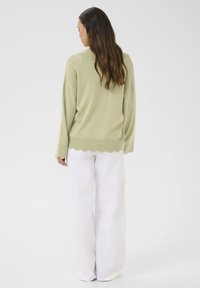 Lichtgroene gebreide trui met een golvende onderrand, gecombineerd met brede witte broek. Zachte textuur en losse pasvorm.