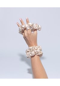 Ensemble de deux chouchous en satin crème, avec un design froncé. Un chouchou est porté au poignet, mettant en valeur sa texture douce et lisse.