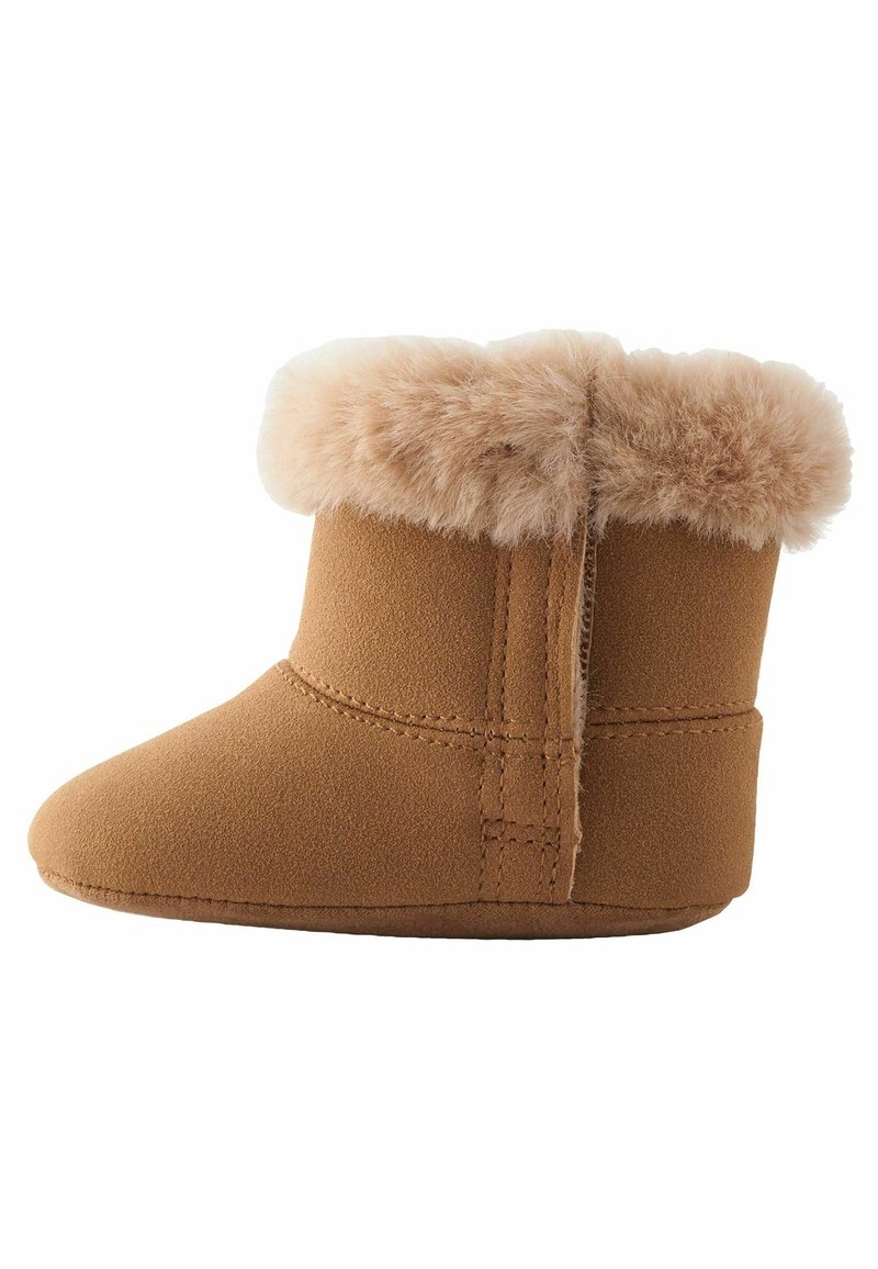 Bottine bébé souple couleur beige avec bordure en fourrure pelucheuse autour de la cheville et coutures visibles sur le côté et la semelle.
