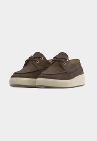 Ζεύγος καφέ σουέντ loafers χωρίς κορδόνια με μπεζ ελαστικές σόλες και  διακοσμητικές λεπτομέρειες με κορδόνια σε λευκό φόντο.