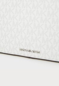 Fehér textúrált anyag, finom monogramos mintával. Az alsó részen ezüst "Michael Kors" márkázás található.