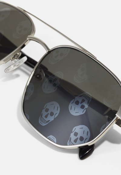 Sunglasses with dark lenses displaying a repeated skull pattern, silver metal frame, and black temple tips. Classic square shape.