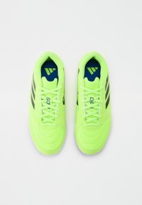 Zapatillas deportivas de un brillante color verde neón con parte superior texturizada, tres franjas oscuras, suelas blancas y plantillas azules con un logo.