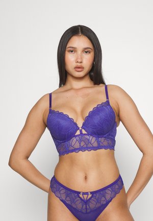 Paarse kanten bralette met gevoerde cups, gebogen randjes en een centraal decoratieve opening; bijpassende kanten string met uitsnijdingen aan de voorkant.