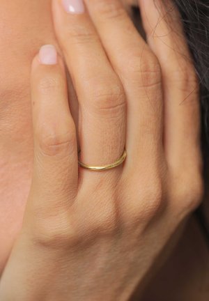 Gylden ring på en finger med en glat, poleret overflade. Designet er enkelt og slankt med et diskret indgraveret mønster.